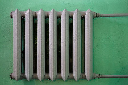 在绿色墙壁上的灰色被绘的铸铁水散热器