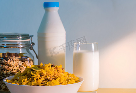一杯牛奶和带有空白标签的牛奶瓶放在木桌上，靠近一碗带勺子的麦片。
