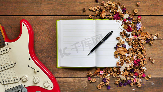 木桌背景上带有笔记本、笔、电吉他和干花的顶视图工作区。
