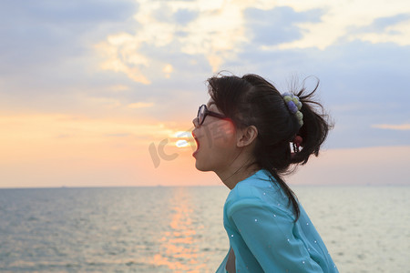 落山的太阳摄影照片_年轻的亚洲女人张开嘴，太阳落山的天空背景