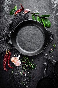 黑色金属烹饪背景上的铸铁锅和香料，从上方看