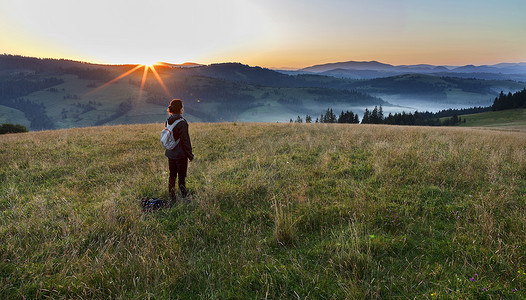 太阳光线摄影照片_一位年轻女子在喀尔巴阡山脉的草甸山上遇见黎明