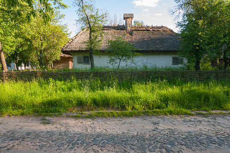 穿过有柳条篱笆和绿色花园的乌克兰老房子附近的石路