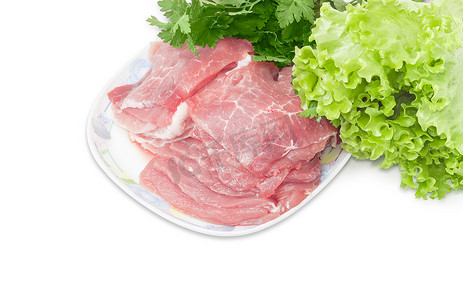 欧芹和莴苣背景下盘子上的生猪肉片