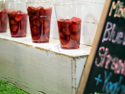塑料玻璃杯中的草莓和糖浆在货架上展示