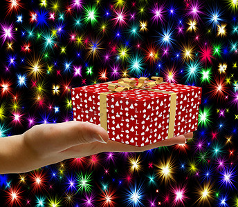 圣诞概念手拿着一个包裹好的圣诞礼盒，在圣诞背景中与五颜六色的星星隔绝地赠送它