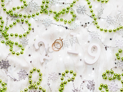 圣诞节和新年背景与数字 2019、绿色装饰、结婚戒指和灯泡。