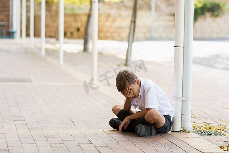 悲观情绪摄影照片_单独坐在走廊的哀伤的男小学生