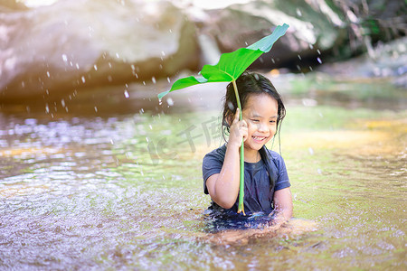 荷叶下的女孩摄影照片_坐在荷叶下玩水的亚洲小女孩
