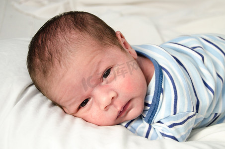 刚出生两周大的男婴醒着躺在白床单上