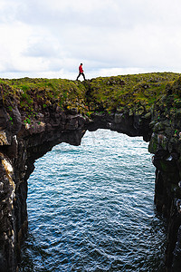 阿尔纳斯塔皮摄影照片_游客走过冰岛 Arnarstapi 的一座天然石桥