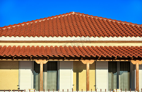 希腊南部一栋乡村传统单层房屋的倾斜浅棕色粘土瓦屋顶指向蓝天中的顶峰。