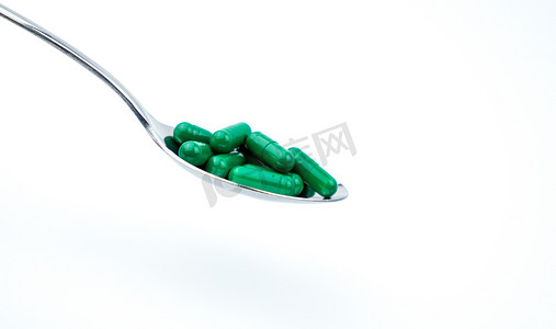 白色背景中分离的不锈钢勺子中的绿色抗生素胶囊药丸，带有文本和剪切路径的复制空间。