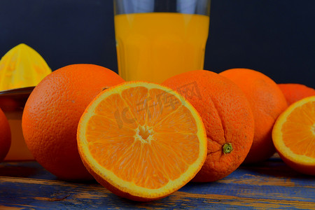 橘子、橙子、一杯橙汁和蓝色木质背景上的手动柑橘榨汁机。
