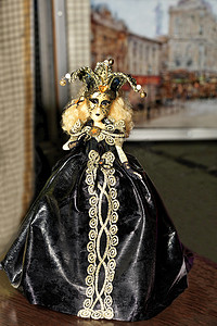 年轻的万圣节女巫玩偶身穿黑色晚礼服，脸上化着深色妆容，头上戴着一顶三角帽。