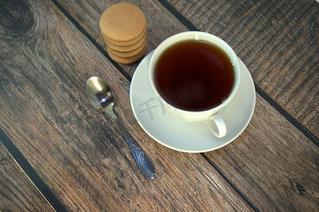 木桌上放着一杯放在瓷碟上的红茶、一把勺子和一堆巧克力海绵饼干。