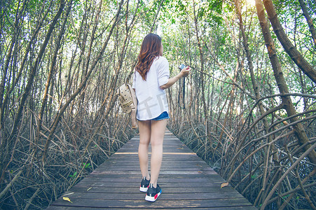 幻灭摄影照片_女孩独自走在木桥上，手拿着相机。