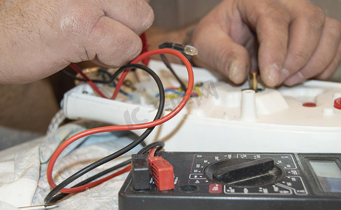 老电工手的特写，使用数字电压表电压修复电熨斗，选择性聚焦