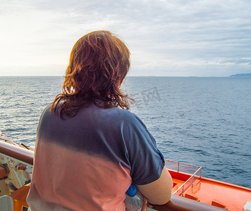 快乐之旅摄影照片_快乐的女人看着海岸线和大海，享受游轮之旅，从后面欣赏风景