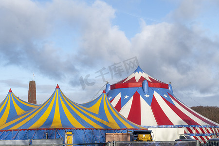 红白相间的马戏团帐篷，顶上是蓝色星光罩，顶着晴朗的蓝天，云朵
