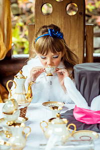 爱丽丝梦游仙境中一个小美女在公园桌边喝茶的前景