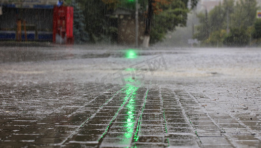 绿色交通灯照亮了人行道和柏油路上的大雨。