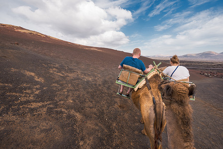 在西班牙加那利群岛兰萨罗特岛 Timanfaya 国家公园的火山景观中无法辨认的游客骑骆驼。