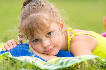 五岁的女孩躺在绿色草地上的床上，抚摸着看着画框