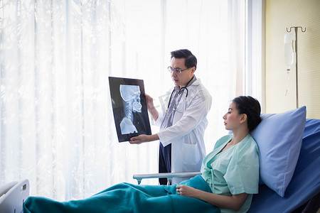 医生正在向躺在医院病床上的女性患者解释脑部 X 光检查结果