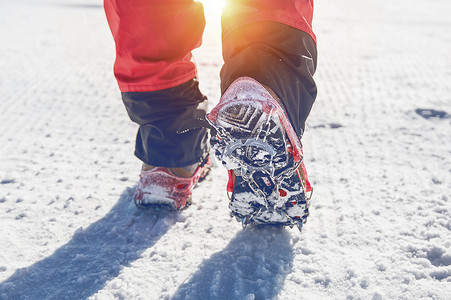 高端装备摄影照片_冬天穿着雪鞋和鞋钉在雪地上行走的景色。