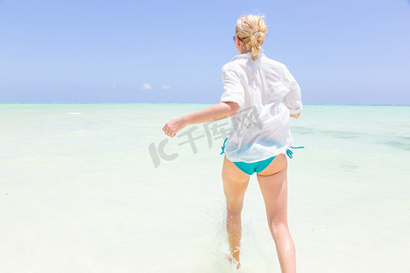 奔跑乌龟摄影照片_年轻活跃的女人在 shellow 海水中奔跑和飞溅很开心。