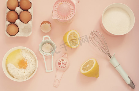 用于烹饪柠檬蛋糕或糖果的配料和厨房烘焙工具 — 鸡蛋、面粉、手动榨汁机、糖，背景为柔和的粉红色。