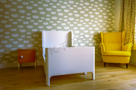 有图案的椅子摄影照片_蹒跚学步的男孩的卧室，墙上有云图案，复古椅子，木地板和橙色床头柜。