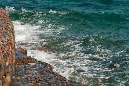 美丽清澈的绿松石海水面照片，石质海景背景上有波纹和明亮的飞溅，水平图片