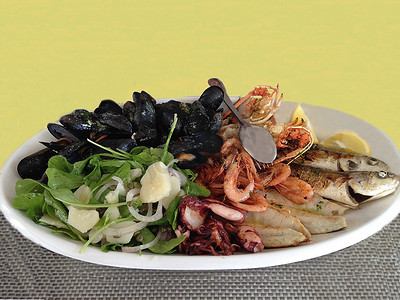 隔离海鲜拼盘：新鲜混合烤贻贝、海螯虾、虾、鱼，在白盘上装饰着芝麻菜、洋葱、柠檬和酱汁。