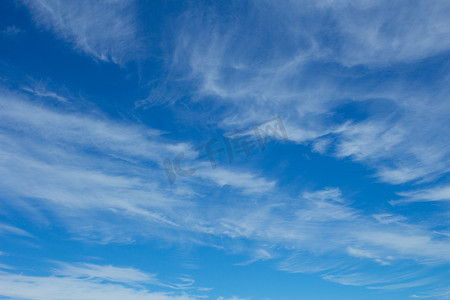 晴朗天空背景摄影照片_明亮的蓝色晴朗的夏日天空上蓬松的白云