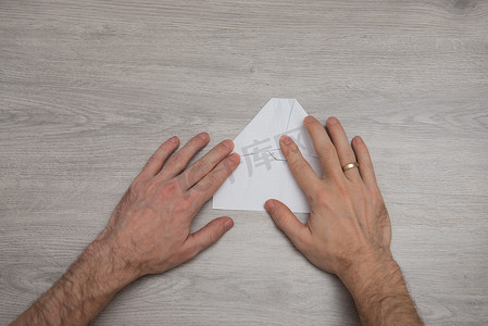 如何在带手臂的木桌上逐步制作折纸纸飞机的照片说明。