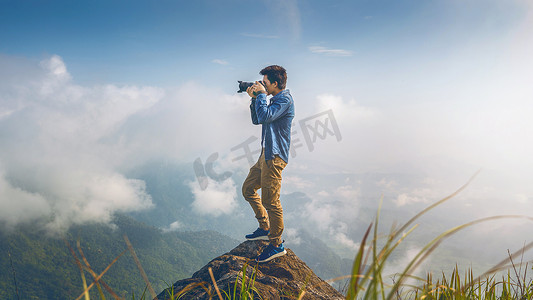 摄影师手持相机，站在大自然中的岩石上。