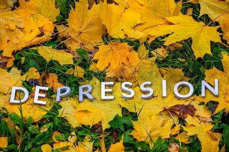 厚摄影照片_抑郁症这个词用铝厚的字母放在地上，上面有枫叶、绿草和复制空间。