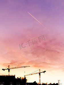 华丽的粉红色、珊瑚色和紫色的夕阳与云彩、飞行的飞机和建筑起重机。