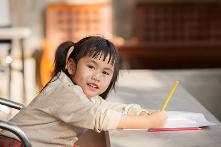 正在学习的学生摄影照片_手拿黄色铅笔做学校家庭作业的亚洲儿童