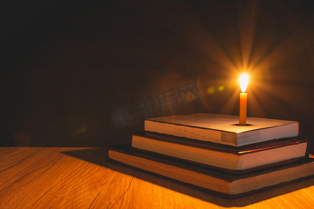 木桌上一堆旧书燃烧蜡烛的特写