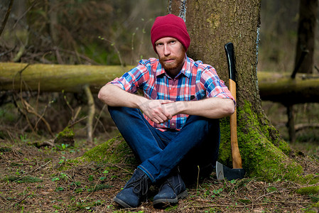 身穿格子衬衫的男子坐在森林里的一棵树旁，护林员