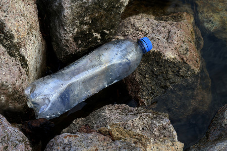 海洋塑料垃圾污染摄影照片_河边废塑料瓶、垃圾污染、垃圾垃圾塑料瓶在石头上倒空