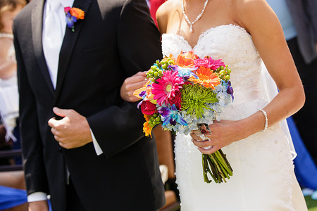 蓝色花束摄影照片_新娘和她的父亲拿着五颜六色的花束走在过道上