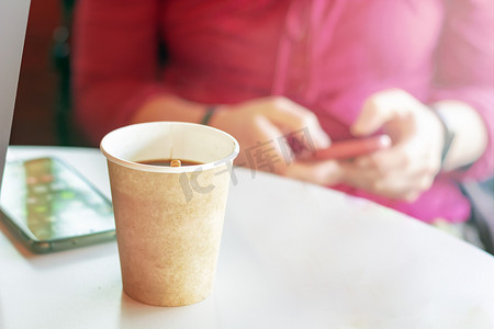 回收纸容器里的咖啡，背景是一个女孩在检查她的智能手机
