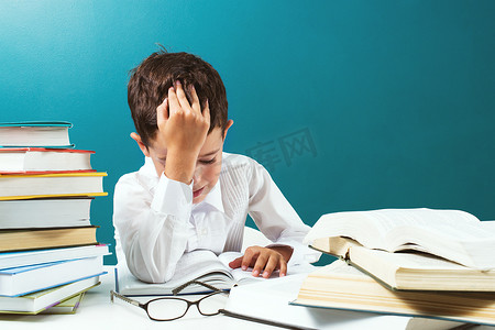 可爱的男孩在桌上阅读困难的书，蓝色背景