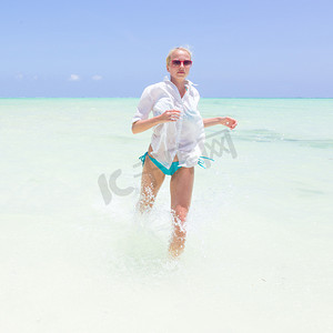 年轻活跃的女人在 shellow 海水中奔跑和飞溅很开心。