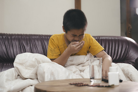 流感关怀摄影照片_家里沙发上打喷嚏的小男孩