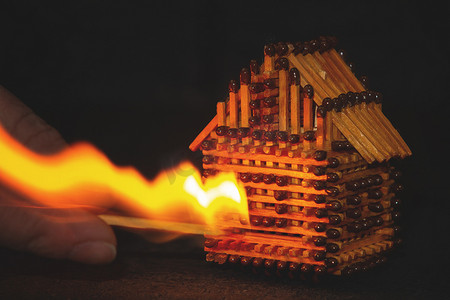 手用燃烧的火柴点燃火柴、风险、财产保险保护或点燃可燃材料概念的房屋模型